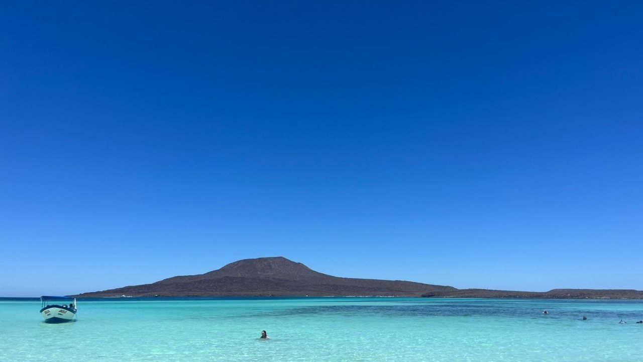 El cono volcánico de Isla Coronado sobre bajos de arena turquesa, con una lancha fondeada frente a la playa